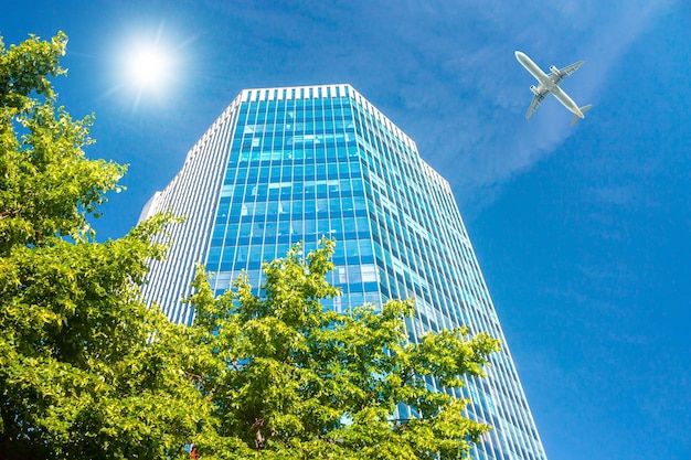 Um arranha-céu de escritório moderno e um avião de passageiros branco sobrevoando este edifício