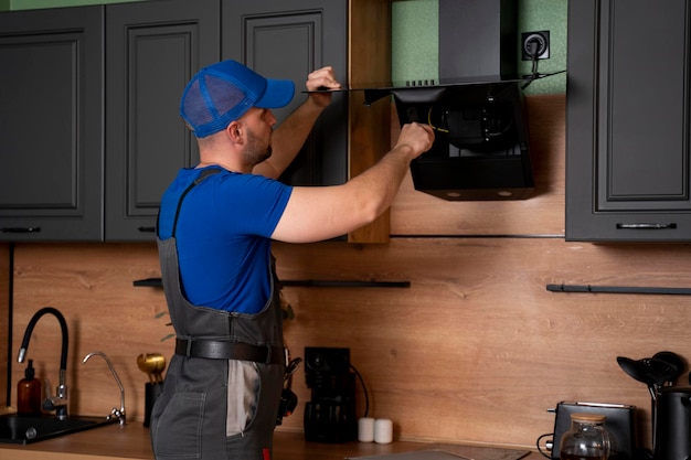 Foto um artesão em uniforme instala ou repara um exaustor de cozinha substitui o filtro no exaustor