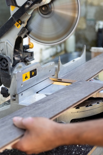 Um artesão serra uma placa de madeira em uma serra circular. Confecção de móveis com ferramenta profissional.