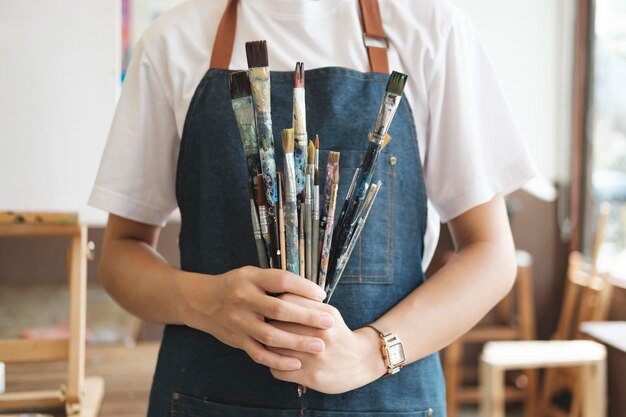 Foto um artista de close-up mãos vestindo um avental manchado com tinta agarrando muitos pincéis e pincéis