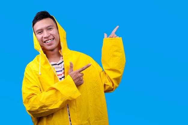 Um asiático alegre vestindo um casaco amarelo mostrando anúncios em espaço de cópia isolado em fundo azul
