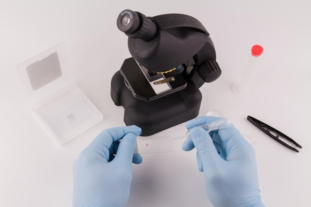 Um assistente de laboratório em luvas médicas azuis trabalha com um microscópio
