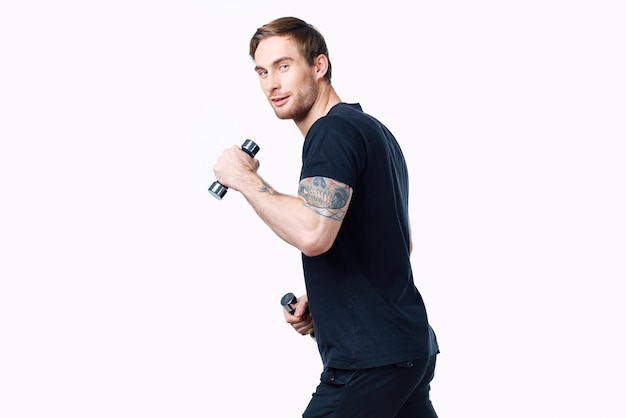 Um atleta em uma camiseta preta com halteres está envolvido em fitness em uma vista lateral de fundo branco