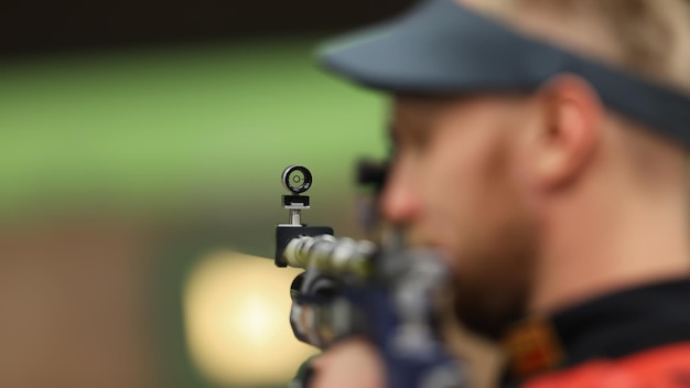 Um atleta masculino atira com um rifle de ar Foco seletivo na mira frontal do rifle