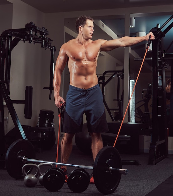 Um atleta musculoso sem camisa fazendo exercício com um expansor no ginásio.