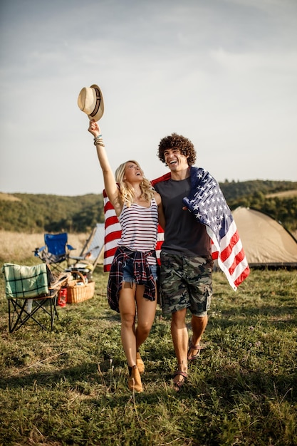 Um atraente casal alegre com bandeira americana festejando no acampamento em um festival ao ar livre.