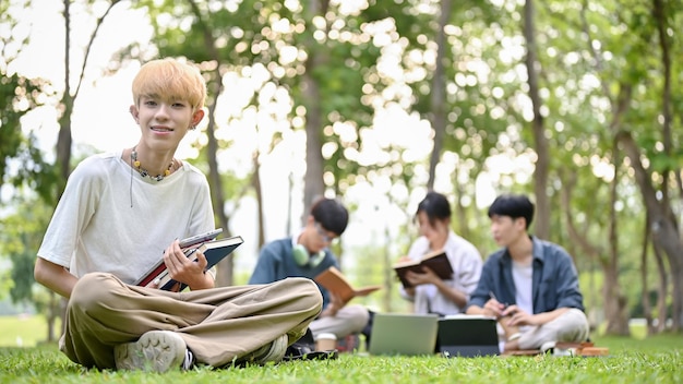 Um atraente jovem estudante gay asiático senta-se em um parque do campus com seus livros escolares