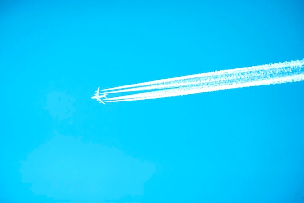 Um avião com quatro linhas claras de rastros contra um céu sem nuvens a graça do voo