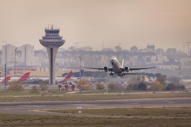 Um avião de passageiros com as turbinas à potência máxima tomando altitude na decolagem perto da torre de controle do Aeroporto Adolfo Suarez Barajas de Madrid, Espanha