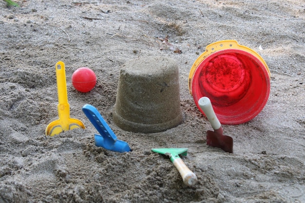 Um balde está na areia ao lado de uma bola vermelha e um brinquedo vermelho horário de verão Brinquedos infantis na praia