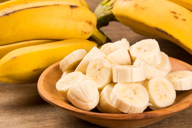 Um banch de bananas e uma banana fatiada em uma panela sobre a mesa.