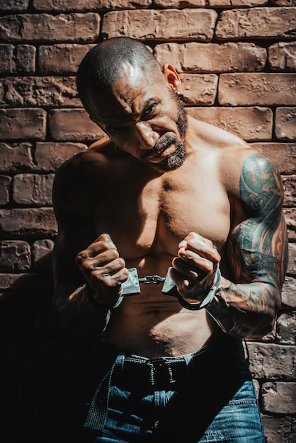 Um bandido ou estuprador em tatuagens é preso em confinamento solitário Mãos algemadas
