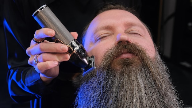 Foto um barbeiro corta a barba de um homem com uma máquina de escrever elétrica fechada