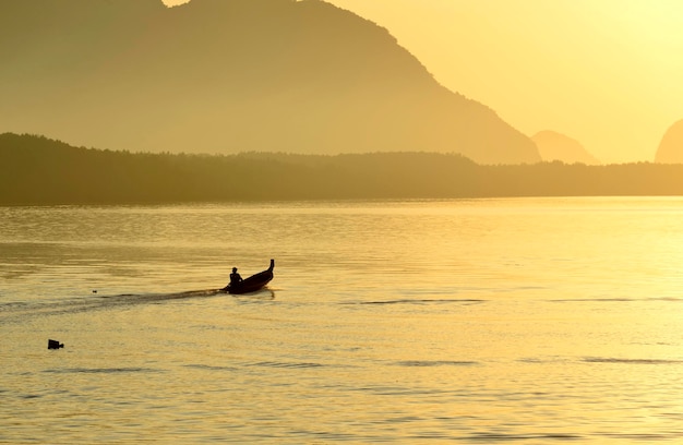 Um barco de pesca à vela na superfície do mar de ouro em uma manhã