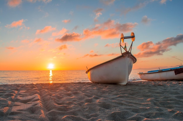 Um barco na praia com o pôr do sol atrás dele