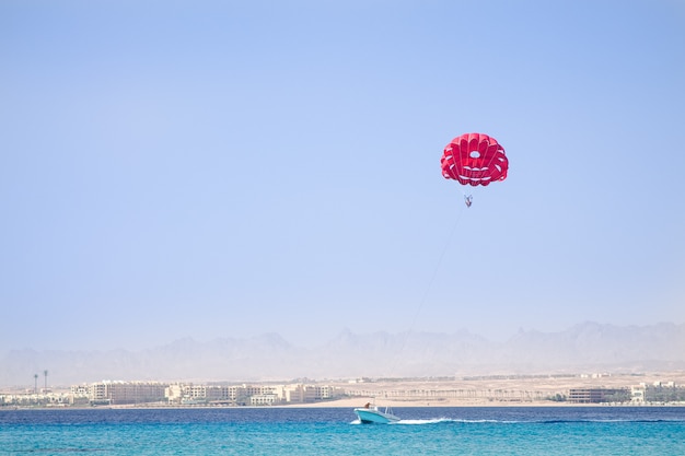 Um barco no mar azul puxa um para-quedas vermelho