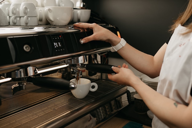 Um barista com avental branco fabricando café expresso em uma máquina de café expresso profissional em uma cafeteria