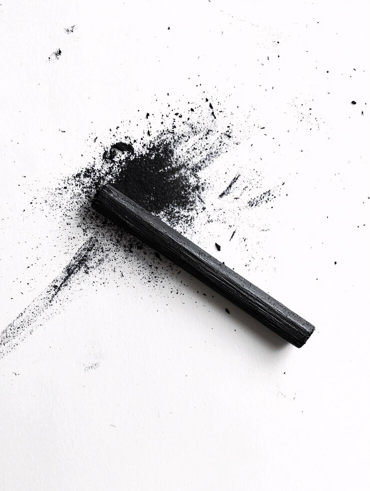 Foto um bastão de carvão texturizado fica contra um fundo branco impecável, destacando sua cor profunda e rica, perfeita para expressão artística
