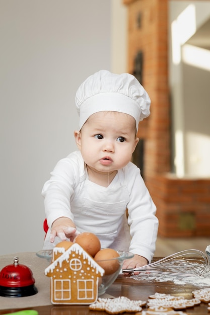 Um bebê asiático com boné e avental de chef faz biscoitos de gengibre de Natal