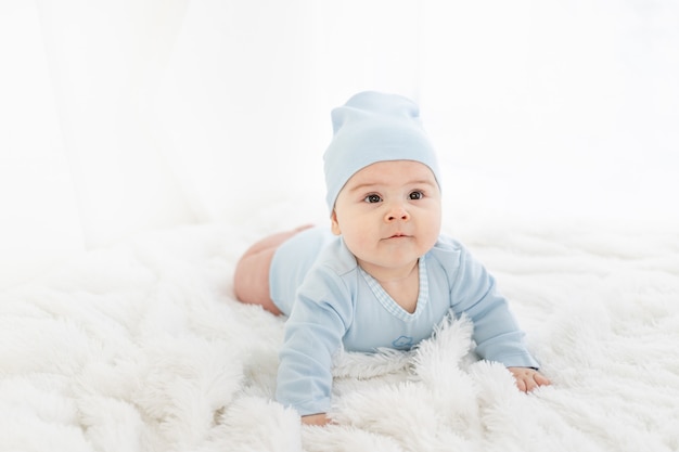 Um bebê com roupas azuis está deitado de bruços em um tapete branco