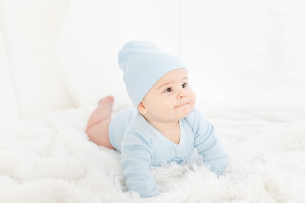 Um bebê com roupas azuis está deitado de bruços em um tapete branco