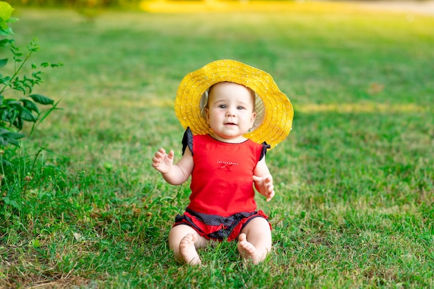 Um bebê com um chapéu amarelo e uma roupa vermelha na grama verde no verão, espaço para texto