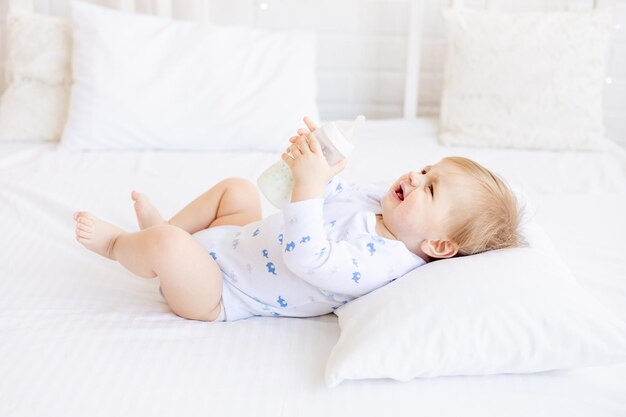 um bebê com uma garrafa de leite não quer comer e chora segurando-a em suas mãos deitado de costas na cama na sala brilhante das crianças o conceito de comida para bebês