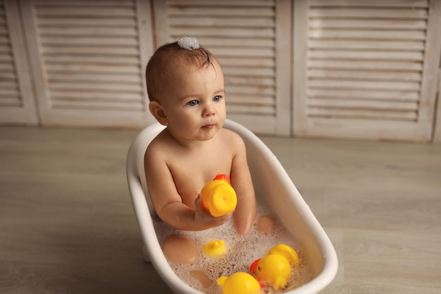 Foto um bebê de 11 meses tomando banho em uma banheira de bebê branca com patinhos de borracha