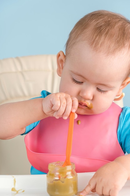 Um bebê de 1217 meses segurando uma colher na mão come brócolis amassado de vegetais de uma jarra de vidro