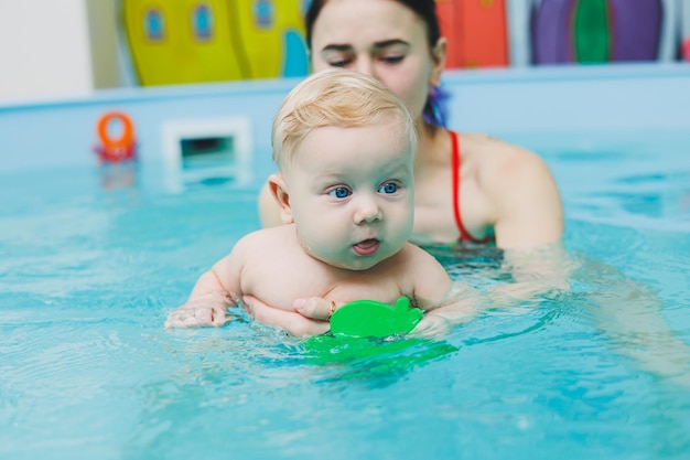Um bebê de 5 meses aprende a nadar em uma piscina com um treinador Bebê aprendendo a nadar