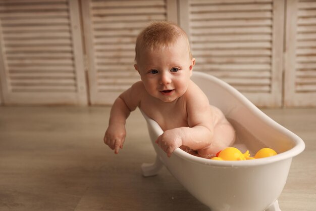 Um bebê de 9 meses tomando banho em uma banheira branca com patinhos de borracha