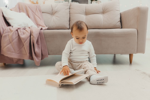 Um bebê de oito meses folheia um livro no chão. retrato de uma criança com um livro.