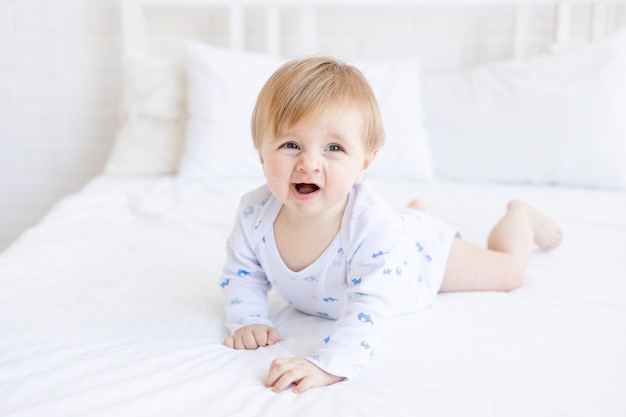 um bebê de seis meses, loiro, quer dormir em um berço, deitado de barriga, em um quarto em casa, com roupas de cama de algodão branco. o conceito de produtos e acessórios para bebês ou sono saudável.