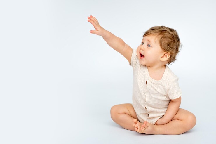 Foto um bebê em um fundo isolado branco com um lugar para o texto em roupas leves uma criança pequena feliz olha e aponta o dedo para o espaço lateral para o texto