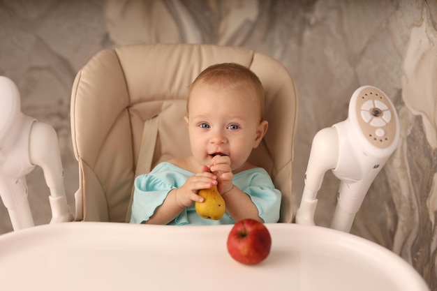 Foto um bebê em uma cadeira de alimentação come uma pêra sozinha