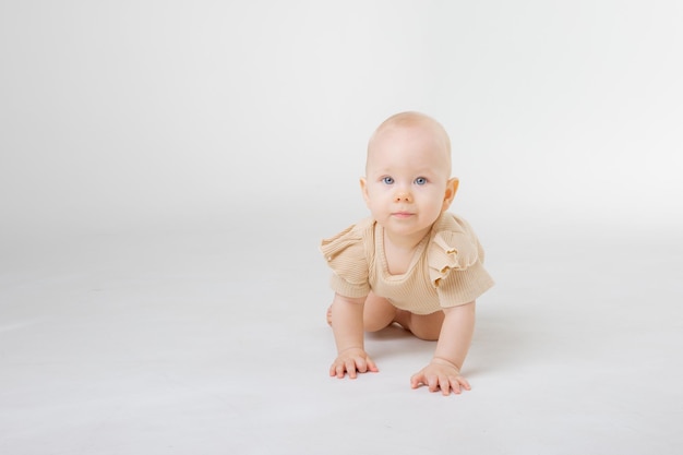 Um bebê em uma roupa bege rasteja em um fundo branco