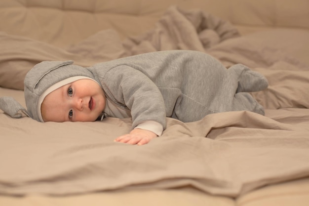 Um bebê em uma roupa cinza está deitado em uma cama com um cobertor que diz bebê nele.