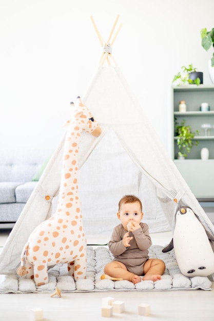 Foto um bebê em uma sala de jogos infantil brilhante com uma tenda e uma girafa brincando com brinquedos de madeira com cubos de desenvolvimento infantil