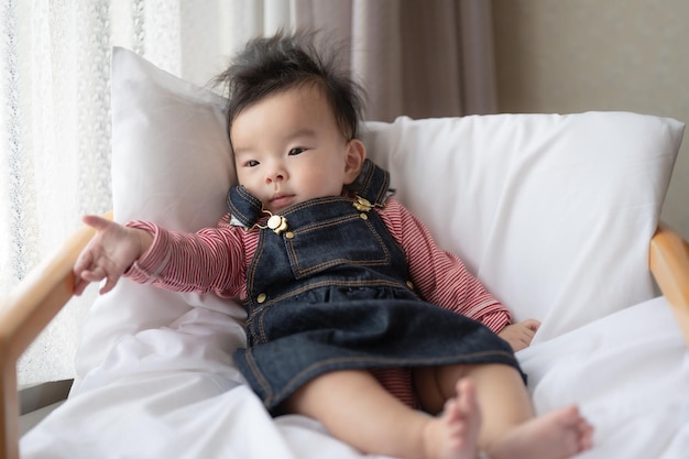 Um bebê está sentado em uma cama com um travesseiro e um chapéu na cabeça.