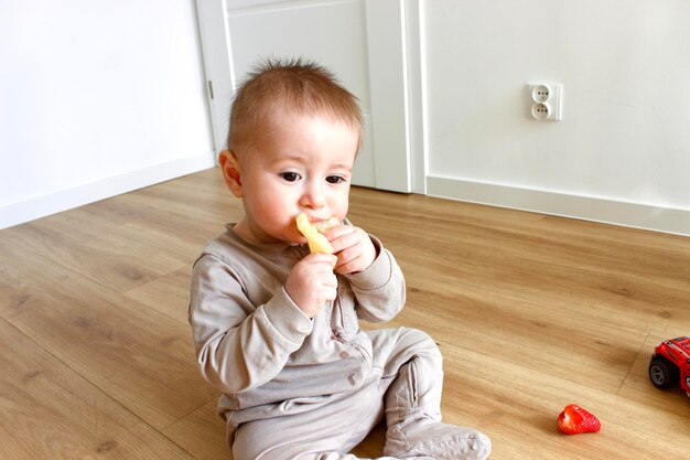 um bebê está sentado no chão e comendo uma banana