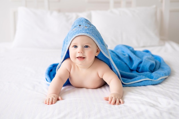 Um bebê fofo e feliz rindo depois do banho está brincando em uma cama branca em um espaçoso quarto infantil A criança está em uma toalha limpa e seca Lavando a higiene do bebê, saúde e cuidados com a pele