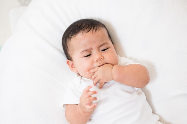 Um bebê fofo em um vestido branco está chorando. Fique com os pais em casa