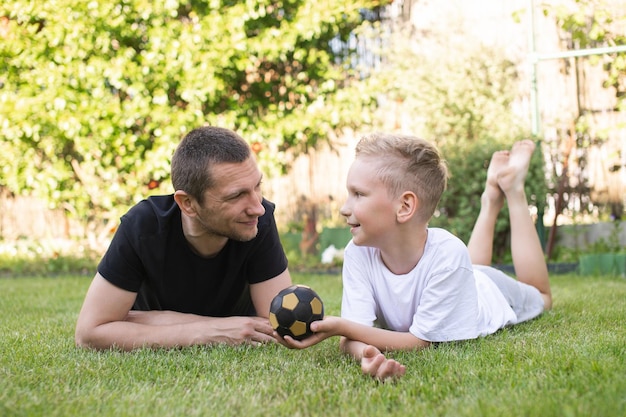 Um bebê fofo está deitado na grama ao lado de seu pai Dê a bola