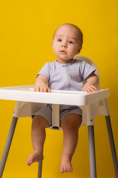 Um bebê fofo está sentado em uma cadeira de criança brincando em um espaço de fundo amarelo para maquete de texto