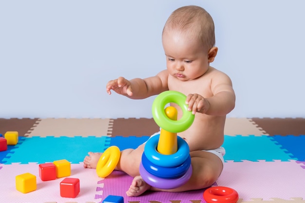 Um bebê recém-nascido está brincando com uma pirâmide multicolorida. uma criança tenta montar uma pirâmide com anéis coloridos.