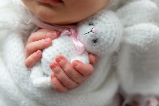 Um bebê segurando um bicho de pelúcia com um laço rosa.