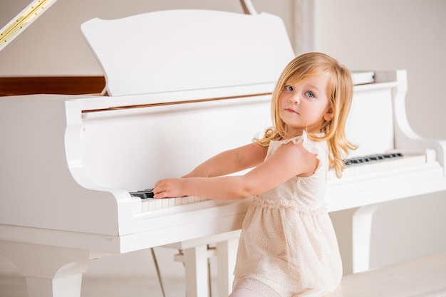 Um bebê toca um grande piano branco em uma sala ensolarada