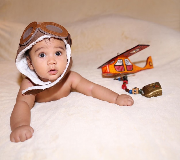 Um bebê usando um chapéu de piloto e deitado em uma cama com um avião de brinquedo ao lado dele