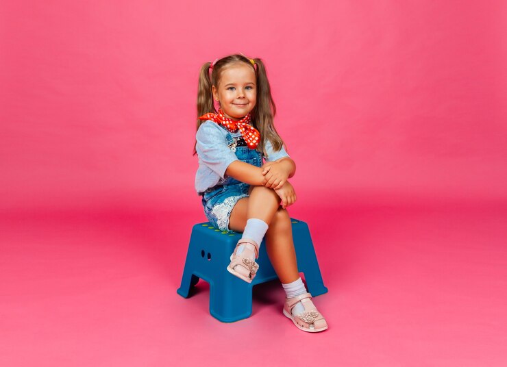 Foto um bebezinho está sentado em uma cadeira sobre um fundo rosa e sorrindo.