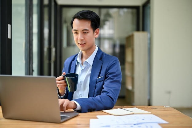 Um belo empresário asiático se concentra em seu trabalho em seu laptop